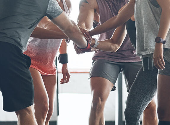 Sportliche Menschen stehen im Kreis und legen die Hände übereinander